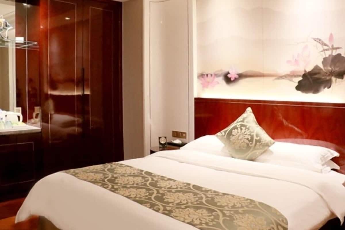 Ein Hotelzimmer mit Bett, Nachttisch, Spiegel und Wand mit floralem Gemälde.