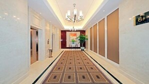 Un couloir d’hôtel avec un tapis à motifs, un lustre et un panneau indiquant le numéro de chambre : 8F.