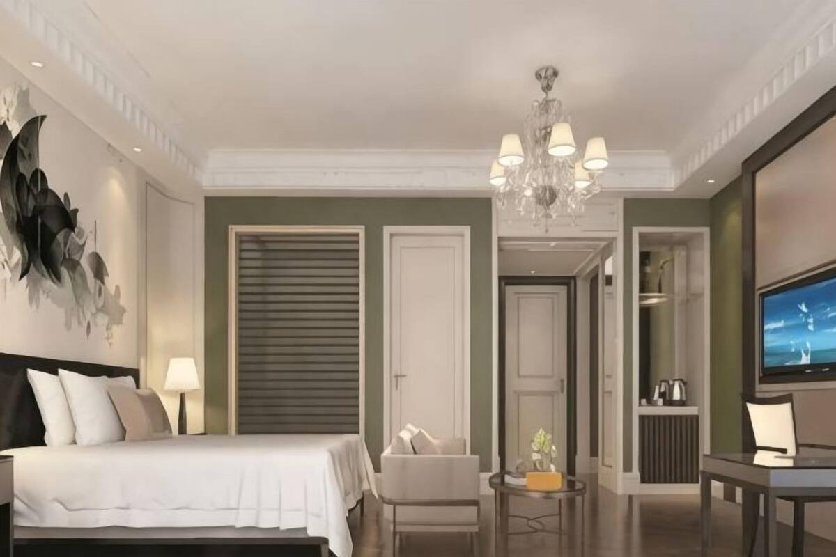 Ein Hotelzimmer mit Bett, Sessel, Tisch, Fernseher und einer Deckenleuchte.