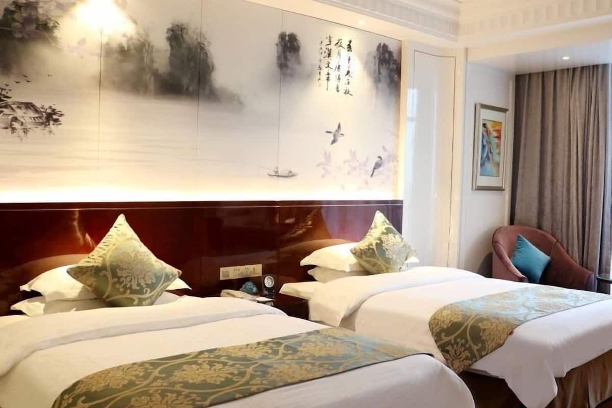 Ein Hotelzimmer mit zwei Betten, einem hölzernen Kopfteil, einem großen Gemälde an der Wand und einem Sessel mit Kissen.