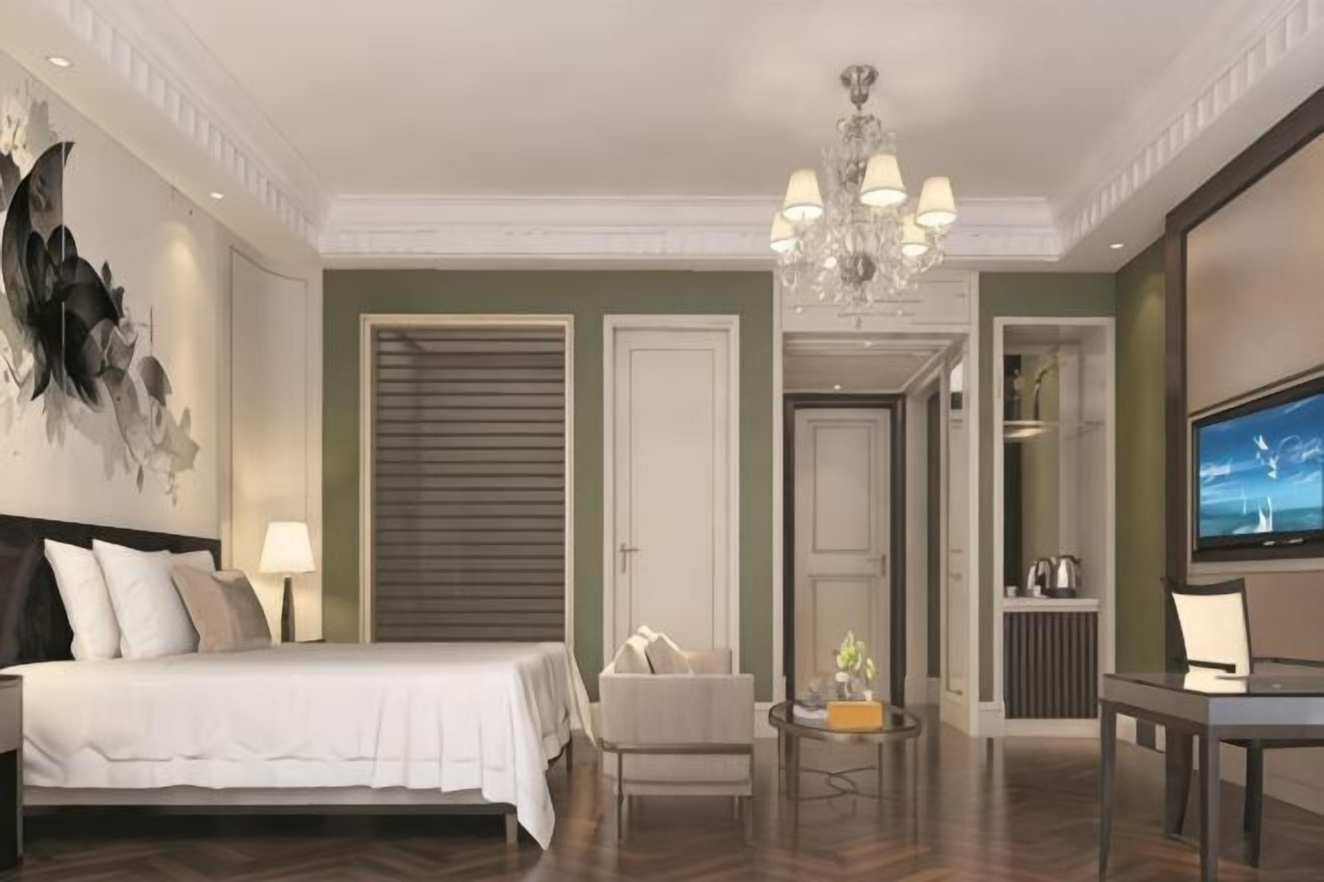 Hotellihuone, jossa on sänky, tuoli, pieni pöytä, televisio ja kattokruunu.