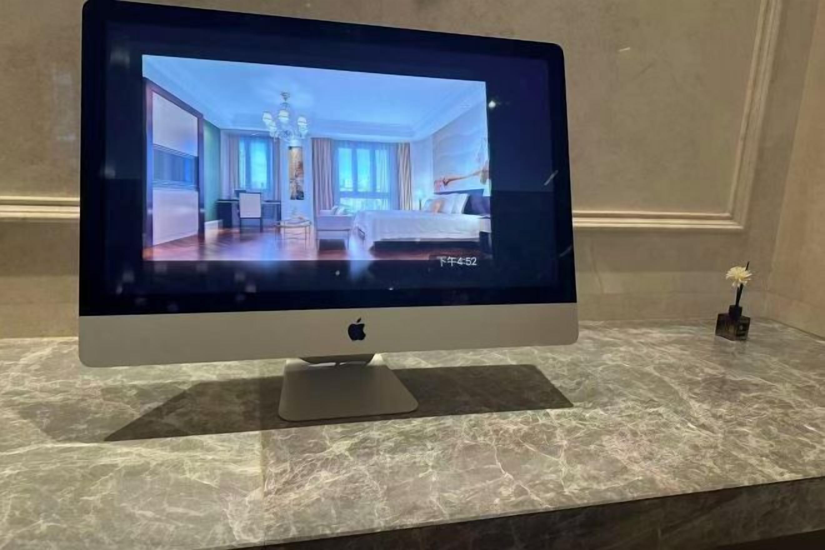 A flat-screen TV on a marble countertop displaying a room with a bed, a desk, and a chair.