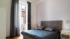 A bedroom with a large bed, a nightstand, a dresser, and a balcony visible through a doorway. - Live Florence Guesthouse (Florence)
