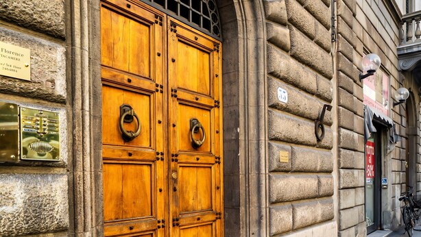 A large wooden double door with metal handles, set in a stone building with plaques and a bicycle parked outside. - Live Florence Guesthouse (Florence)