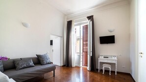 A room with a sofa, a small table, a TV, and a door leading to an outdoor area. - Live Florence Guesthouse (Florence)