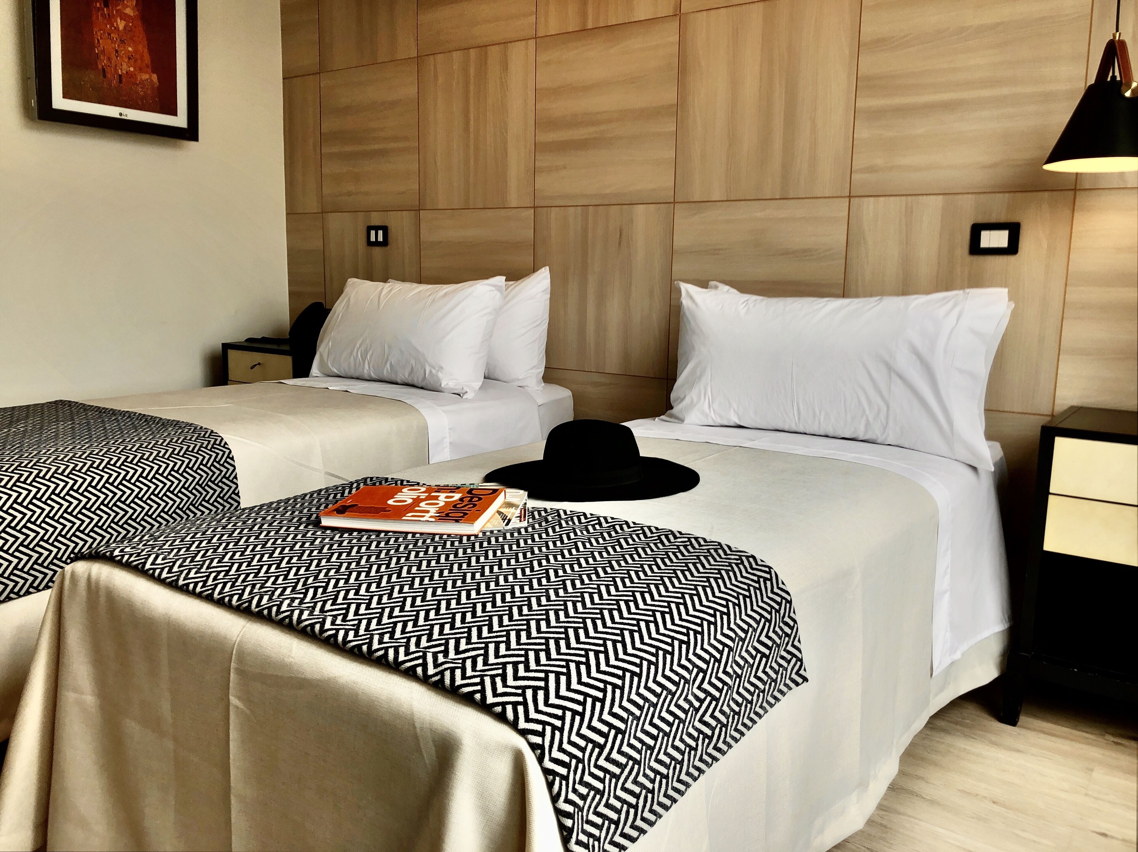 A hotel room with two beds, each with a patterned bedspread, a black hat, and a book titled "Design Group".