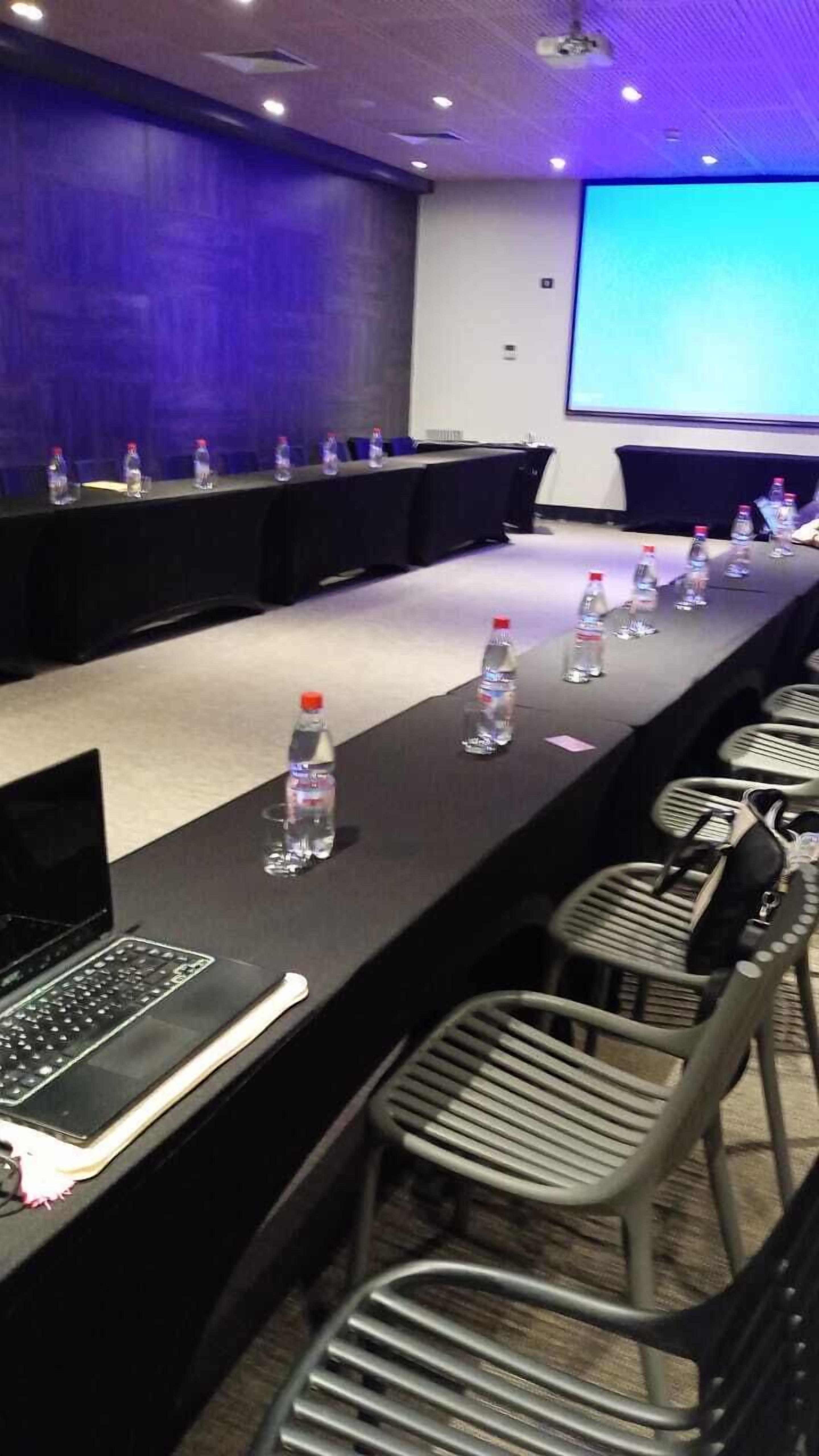 Une salle de conférence avec une longue table, des ordinateurs portables, des bouteilles d’eau et des chaises.
