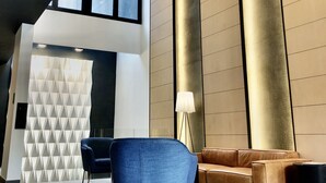 A modern lobby with a blue chair, a brown sofa, and a geometric wall design. - RQ Santa Magdalena (Santiago)