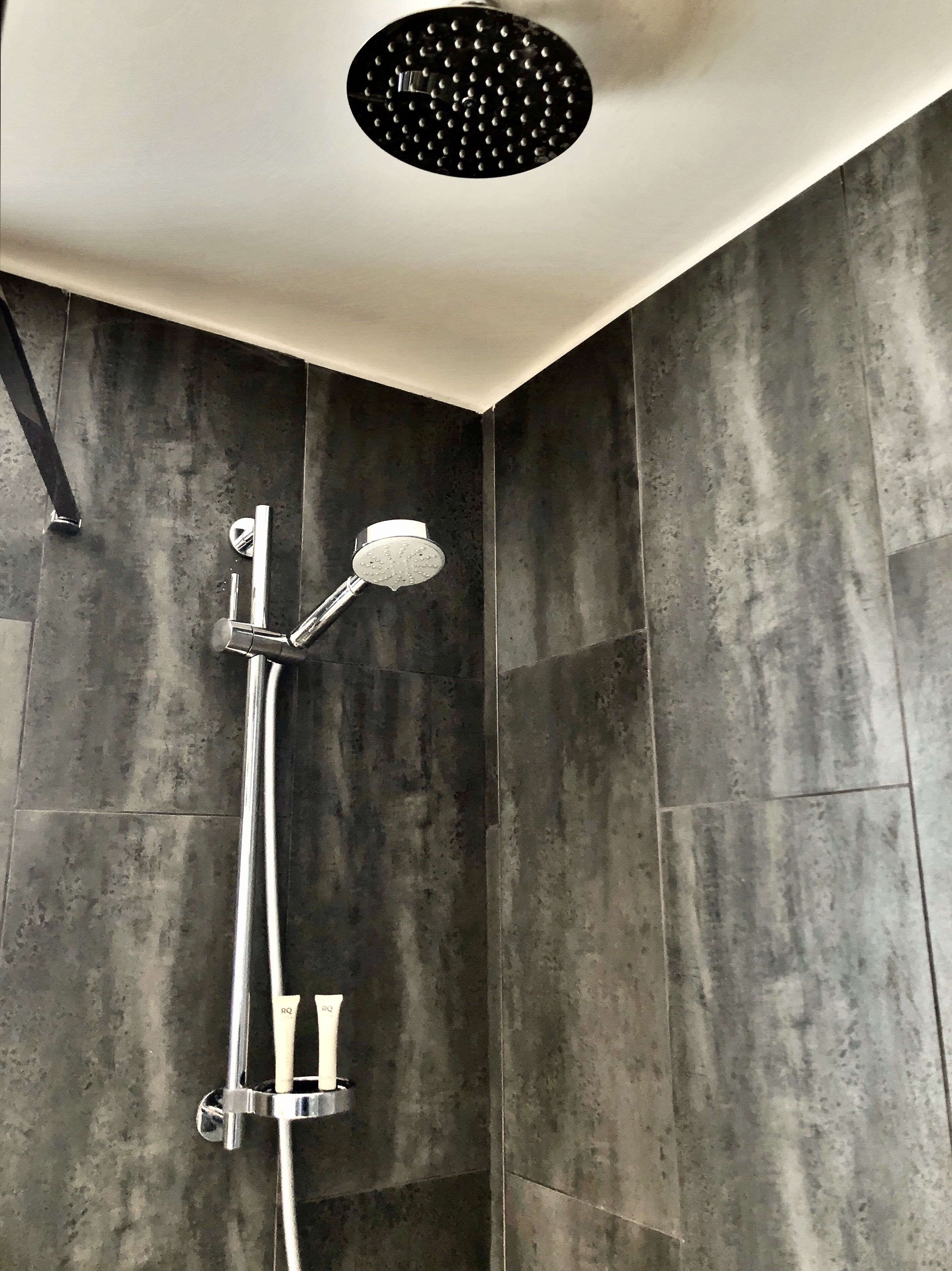 A modern shower with a rain showerhead, chrome fixtures, and a textured wall.