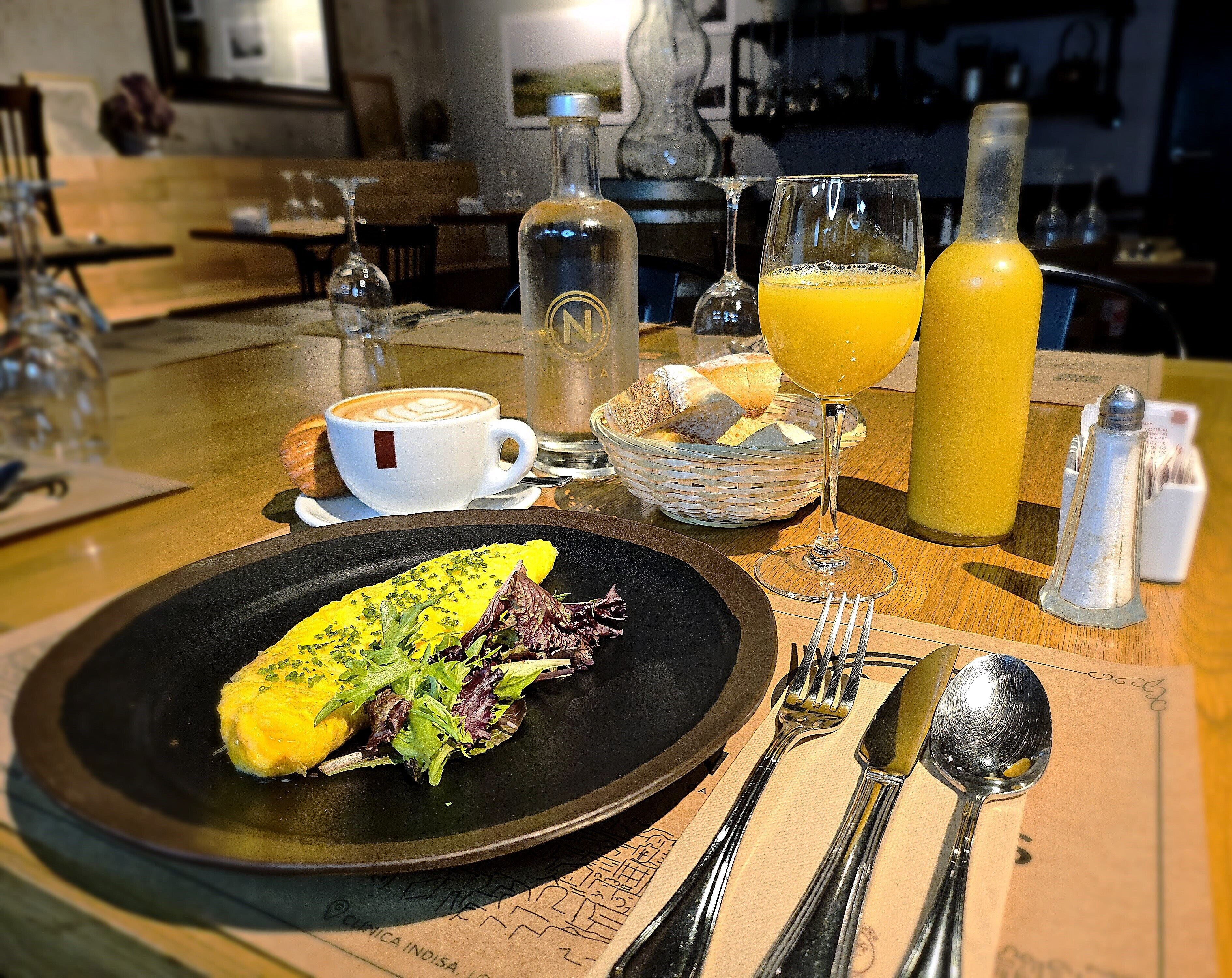 Une table à manger avec une assiette de nourriture, une tasse de café, un verre de jus d’orange et une bouteille d’eau.