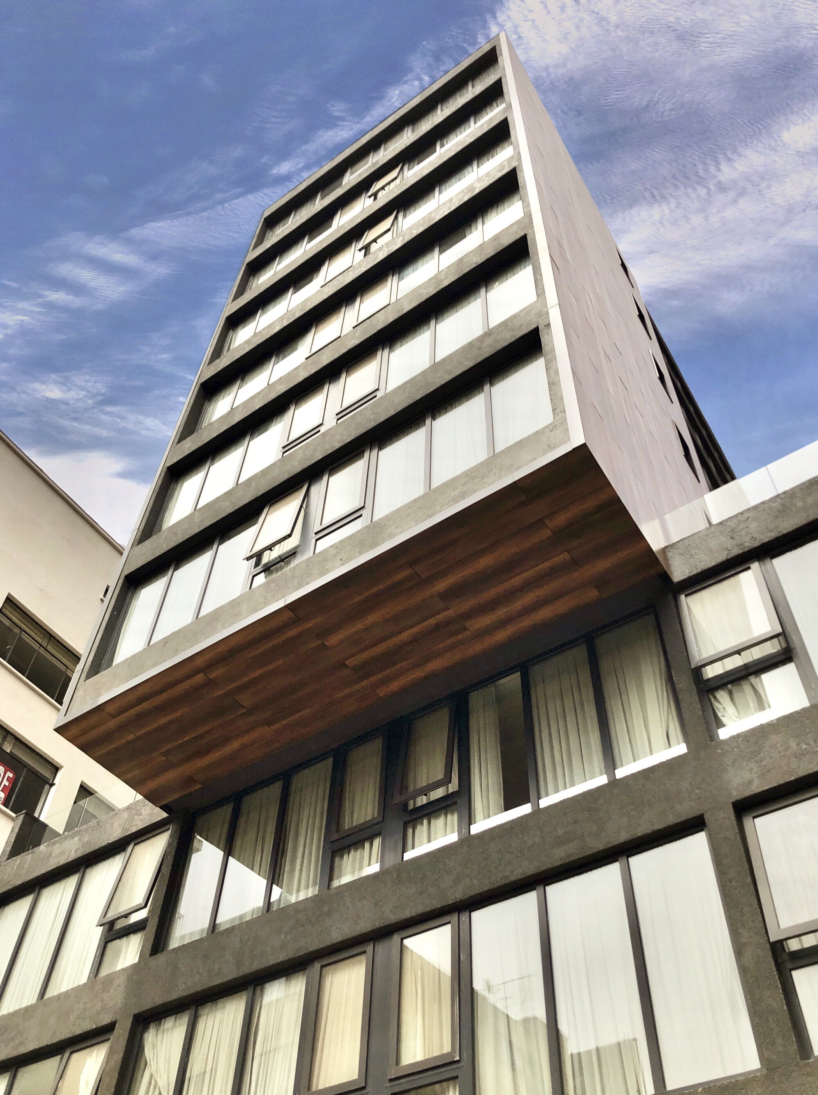Un moderno edificio de gran altura con un balcón de madera llamativo y ventanas amplias.