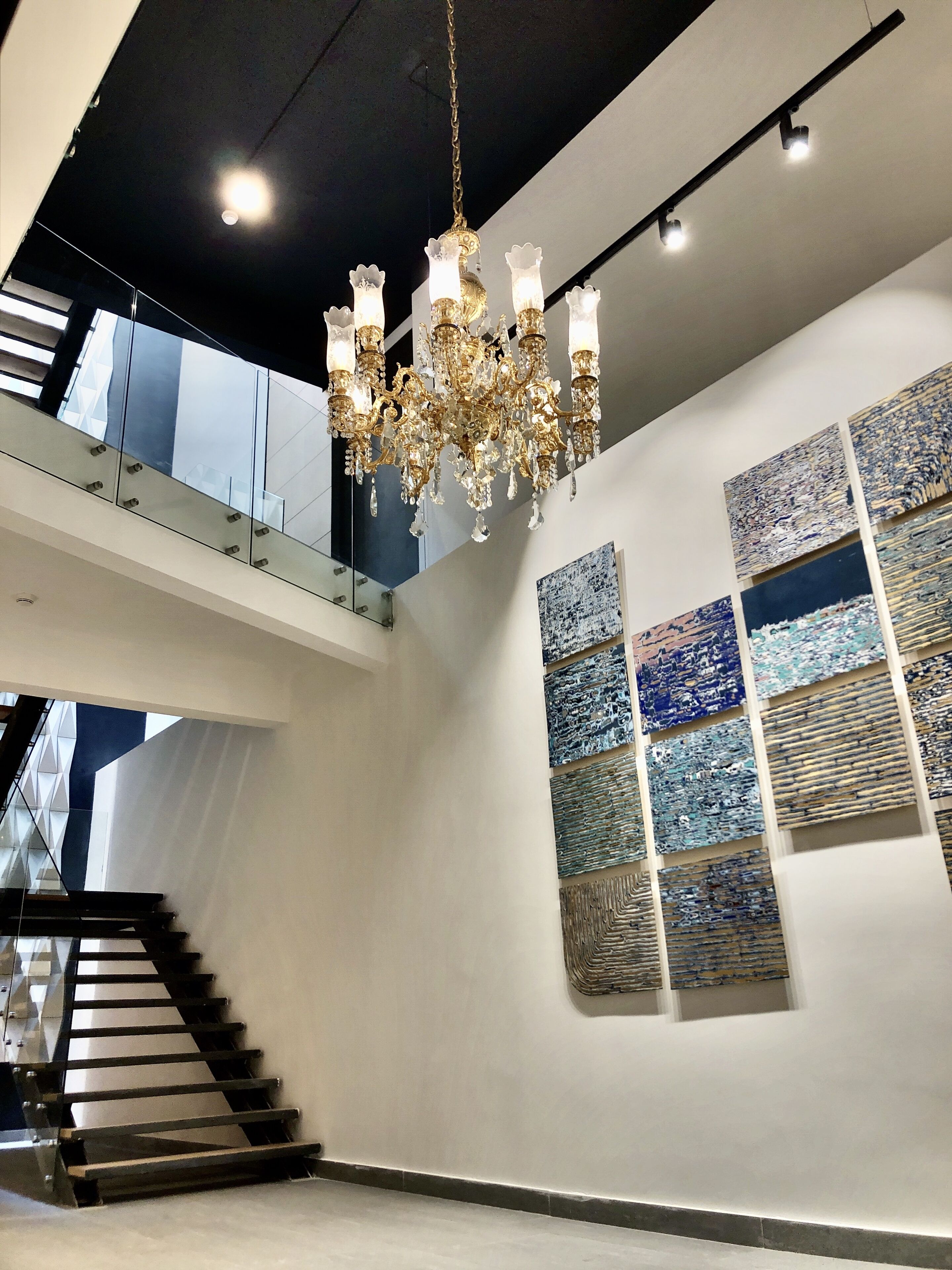 A modern interior with a grand chandelier, a staircase, and abstract wall art.