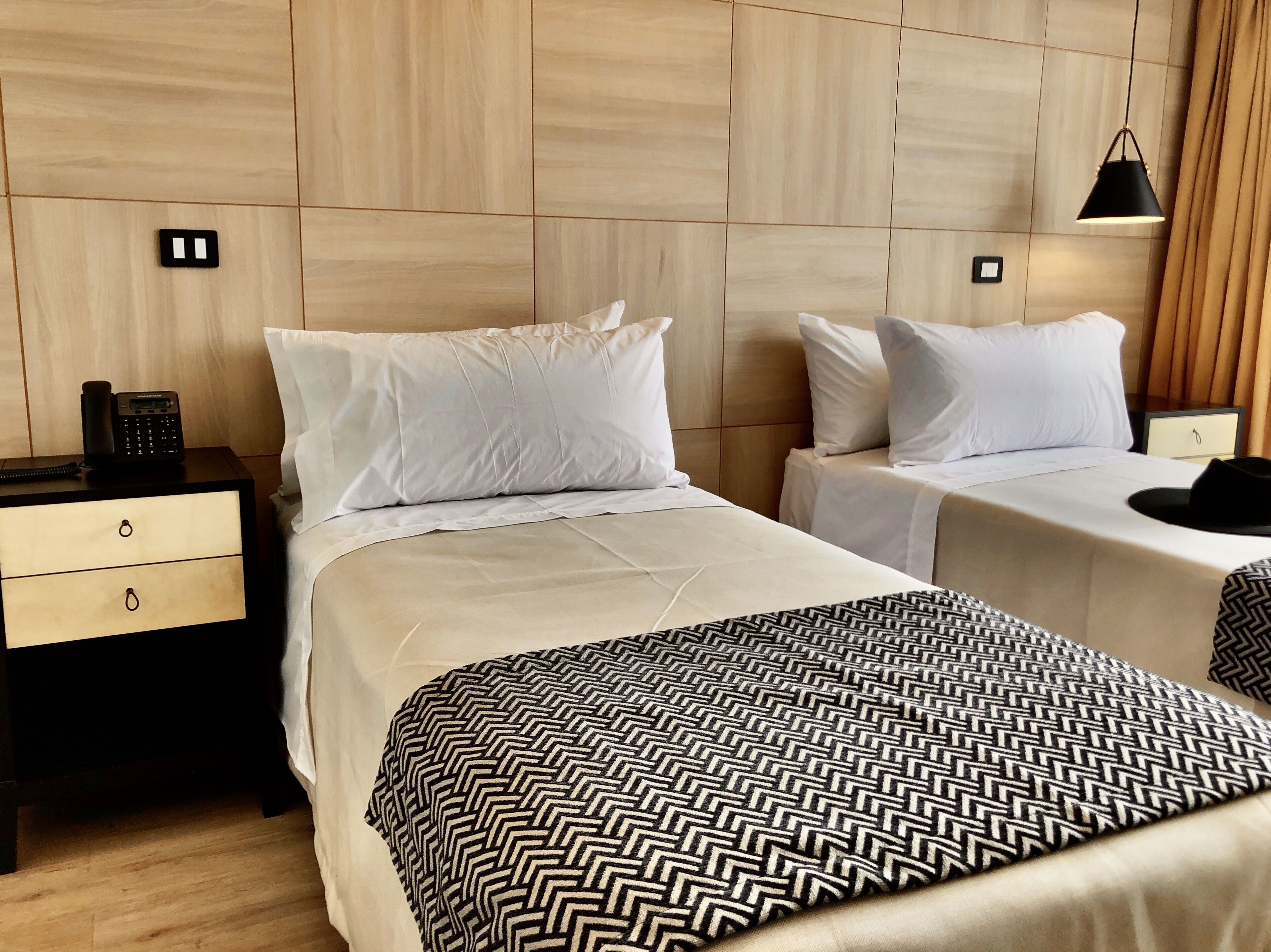 Habitación de hotel con dos camas, una mesita de noche con teléfono y una lámpara.