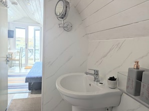 A bathroom with a white sink, a mirror, and toiletries. - Pod Beag Beside the Sea, Isle of Eriskay (Eriskay)