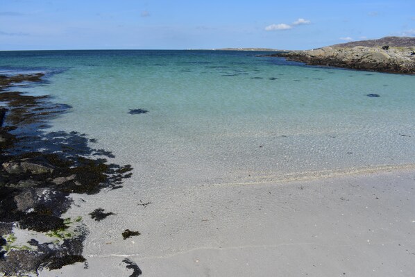 A beach with clear water, rocky shoreline, and distant hills. - Pod Beag Beside the Sea, Isle of Eriskay (Eriskay)