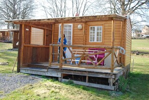 A wooden cabin with a porch, a door, and a window. - Camping La Chevauchée (Bussière-Dunoise)