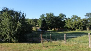 A fenced rural property with a house in the background, surrounded by trees and open fields. - Camping La Chevauchée (Bussière-Dunoise)