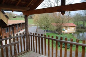 A wooden balcony with a view of a rural area, including a pond and buildings. - Camping La Chevauchée (Bussière-Dunoise)