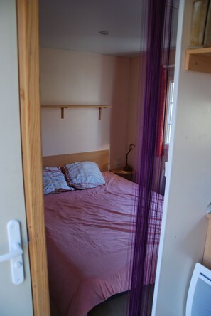 A bedroom with a bed, a nightstand, a lamp, and a window. - Camping La Chevauchée (Bussière-Dunoise)