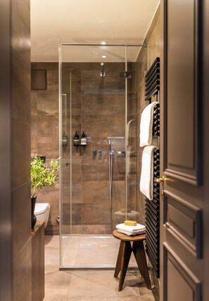 A modern bathroom with a glass-enclosed shower, a wooden stool with a towel, and a bottle of soap. - The Hamlet (Geneva)
