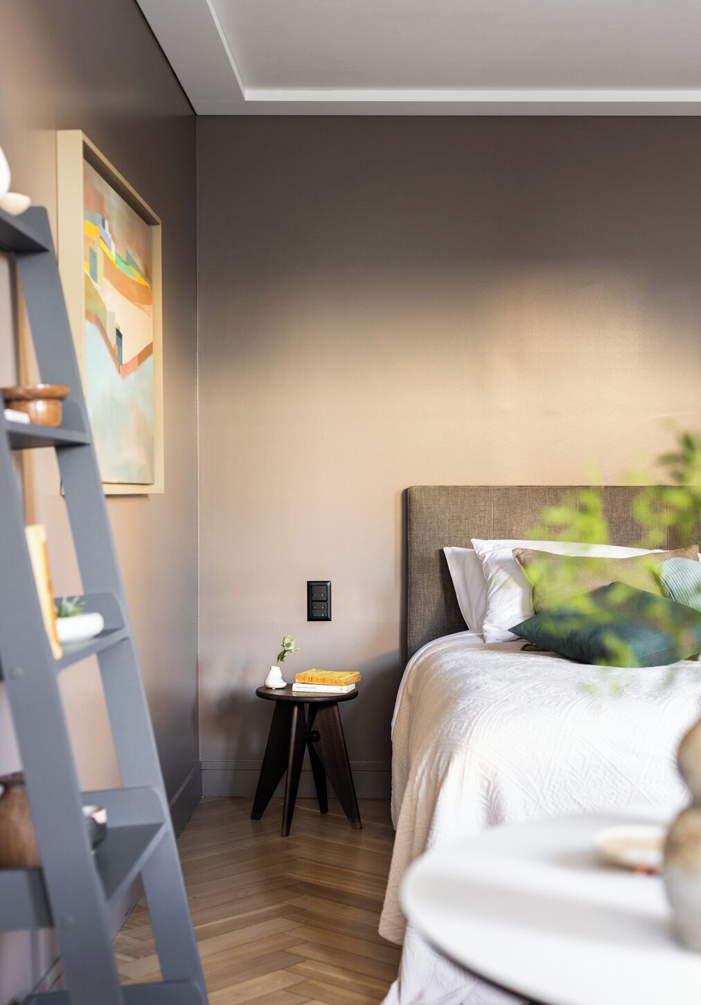 Un dormitorio moderno con cama, mesita de noche, escalera y un cuadro en la pared.
