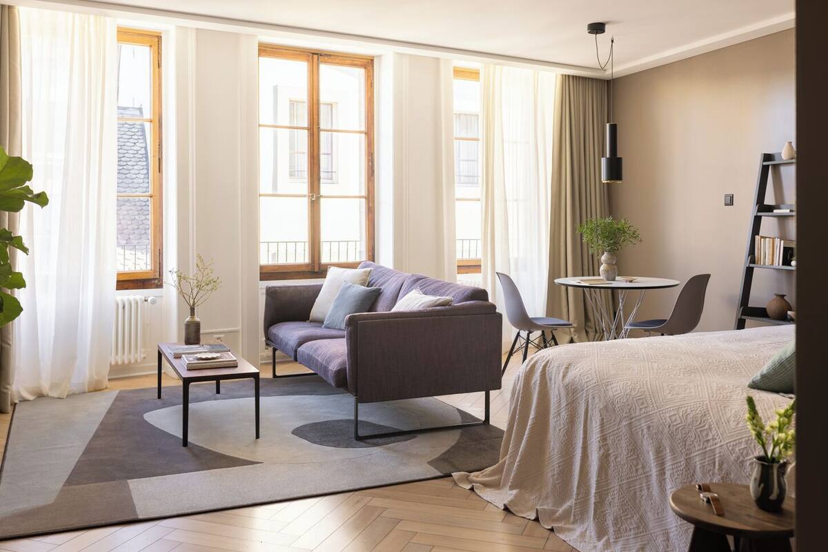 A modern hotel room with a sofa, a small table, a bed, and a chair.