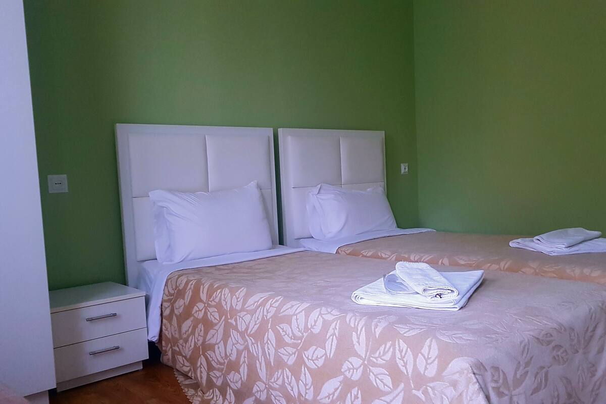 A room with two beds, each with a headboard, a nightstand, and a drawer.