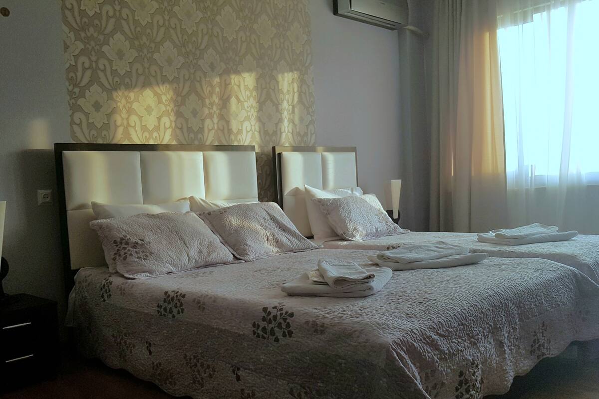 A hotel room with a large bed, two bedside tables, and a window with curtains.