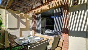 Une terrasse extérieure avec une table dressée pour deux personnes, une colonne en briques et une fenêtre avec des stores.
