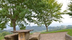 A stone bench with a table in a park setting, surrounded by trees and a paved path. - Hotel Garaiko Landetxea (Garai)