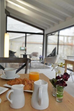 A breakfast setup with croissants, orange juice, and coffee on a wooden table in a modern room with large windows. - Hotel Garaiko Landetxea (Garai)