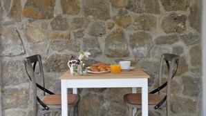 A stone wall, a wooden table, two chairs, a vase with flowers, a plate of croissants, a glass of orange juice, and a cup. - Hotel Garaiko Landetxea (Garai)