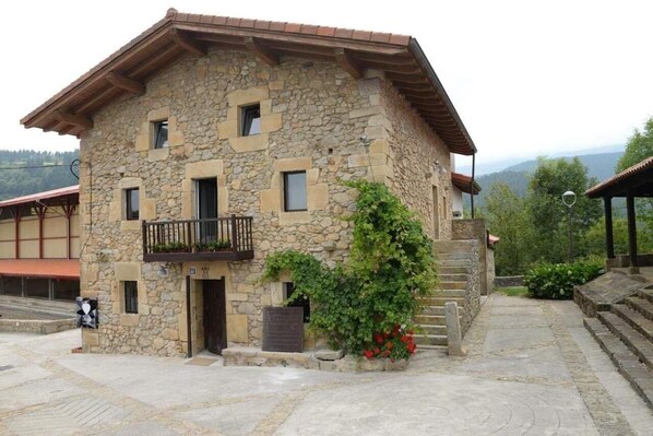 A stone building with a balcony, a door, and steps leading to a covered area. - Hotel Garaiko Landetxea (Garai)