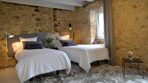 A room with two beds, stone walls, a small table with a vase, and a window with curtains. - Hotel Garaiko Landetxea (Garai)
