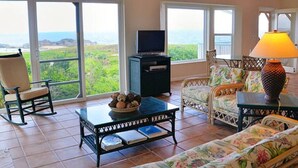 Ein Wohnzimmer mit Fernseher, einem Couchtisch mit Obstschale und einer Couch mit floralen Kissen.