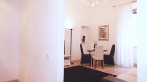 A modern living room with a dining area, featuring a black rug, white walls, and a chandelier. - Ludovisi Decò (Rome)