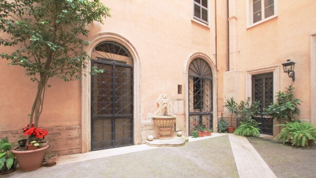 A courtyard with a fountain, potted plants, and a building with arched windows and doors. - Ludovisi Decò (Rome)