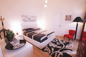 A bedroom with a bed, bedside table, lamp, chair, and artwork on the wall. - Ludovisi Decò (Rome)