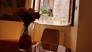 Una habitació amb finestra, un ram de flors en un vas i una cadira de vimet.