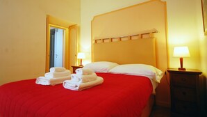 Habitació d'hotel amb una colcha vermella, dos coixins blancs, un capçal de llit de fusta, dues làmpades de nit i un llit ben fet amb tovalloles pliegades.