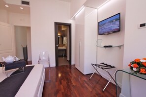 Una habitación de hotel moderna con suelo de madera, un televisor de pantalla plana montado en la pared, una mesa de cristal con un arreglo floral y una silla.