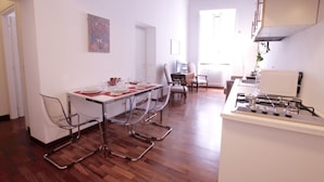 A modern kitchen with a gas stove, a dining area with a table set for four, and a living area with a sofa and a chair. - Monticelli Viola (Rome)