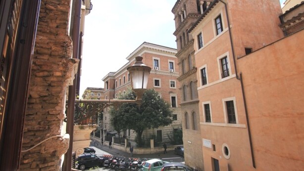A narrow street with parked cars and a building with a stone facade. - Monticelli Viola (Rome)
