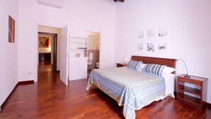 A bedroom with a wooden bed, a nightstand, a bedside table, and a wardrobe. There is a door leading to another room. - Monticelli Viola (Rome)