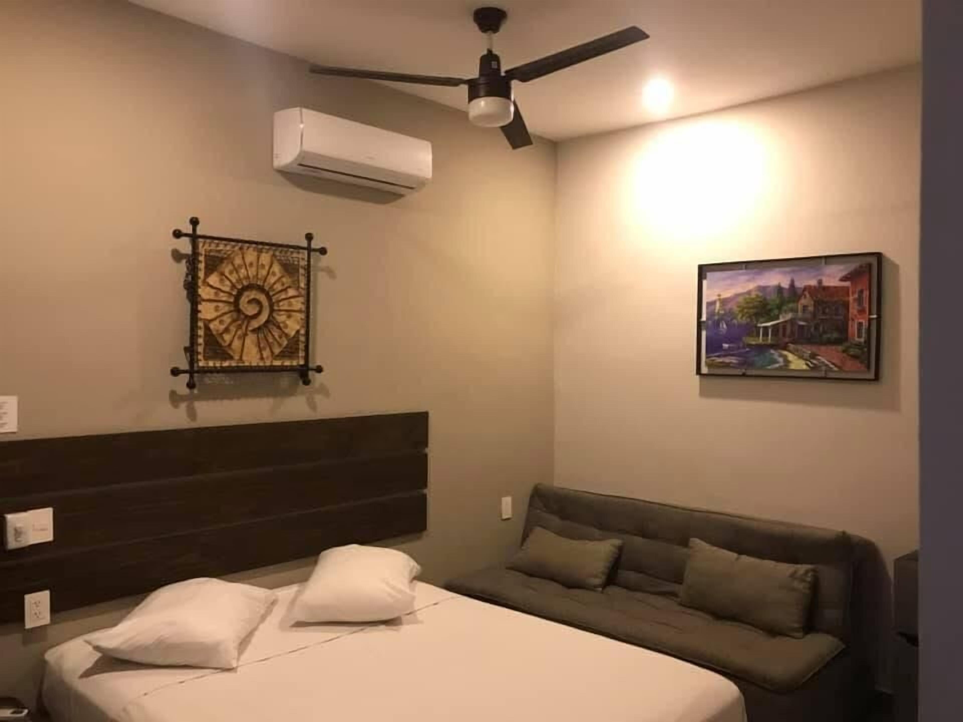 Une chambre d’hôtel comprenant un lit, un canapé, un ventilateur de plafond, un climatiseur, une horloge murale et un tableau.