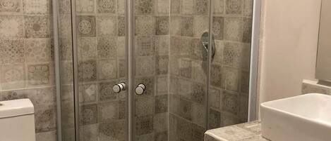 A bathroom with a glass-enclosed shower, a toilet, and a sink.