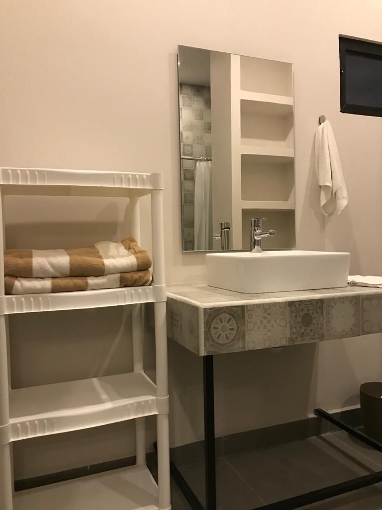 Un baño con lavamanos blanco, espejo y barra para toallas.