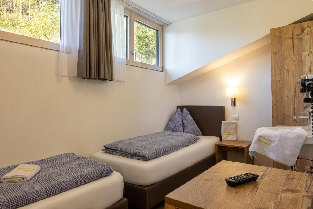 A hotel room with two beds, a wooden table, a remote control, and a window with curtains.