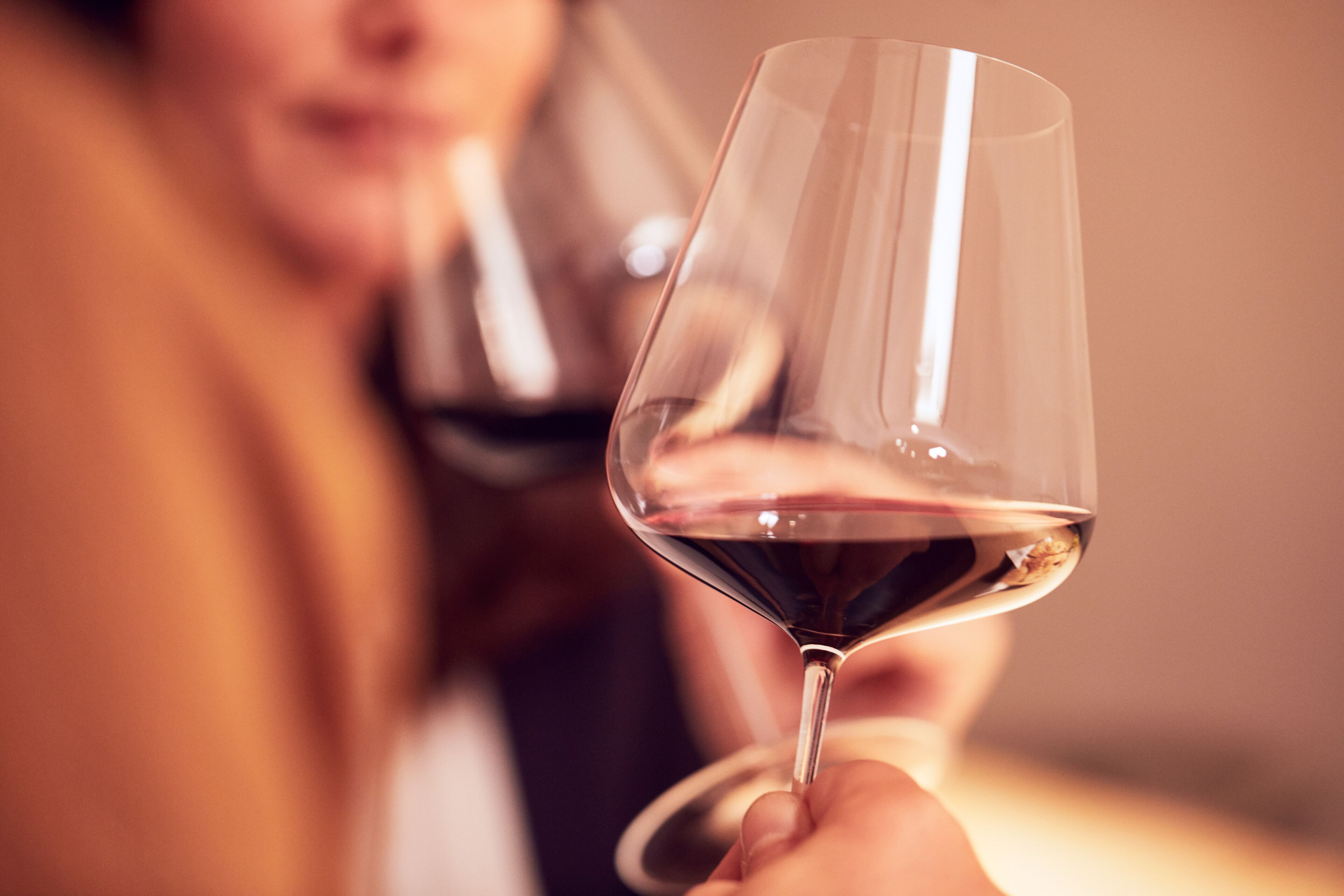 Um close-up de uma taça de vinho sendo segurada por uma pessoa.