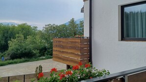 Een modern gebouw met een houten balkon, uitzicht op groen en bergen, en een heldere lucht.